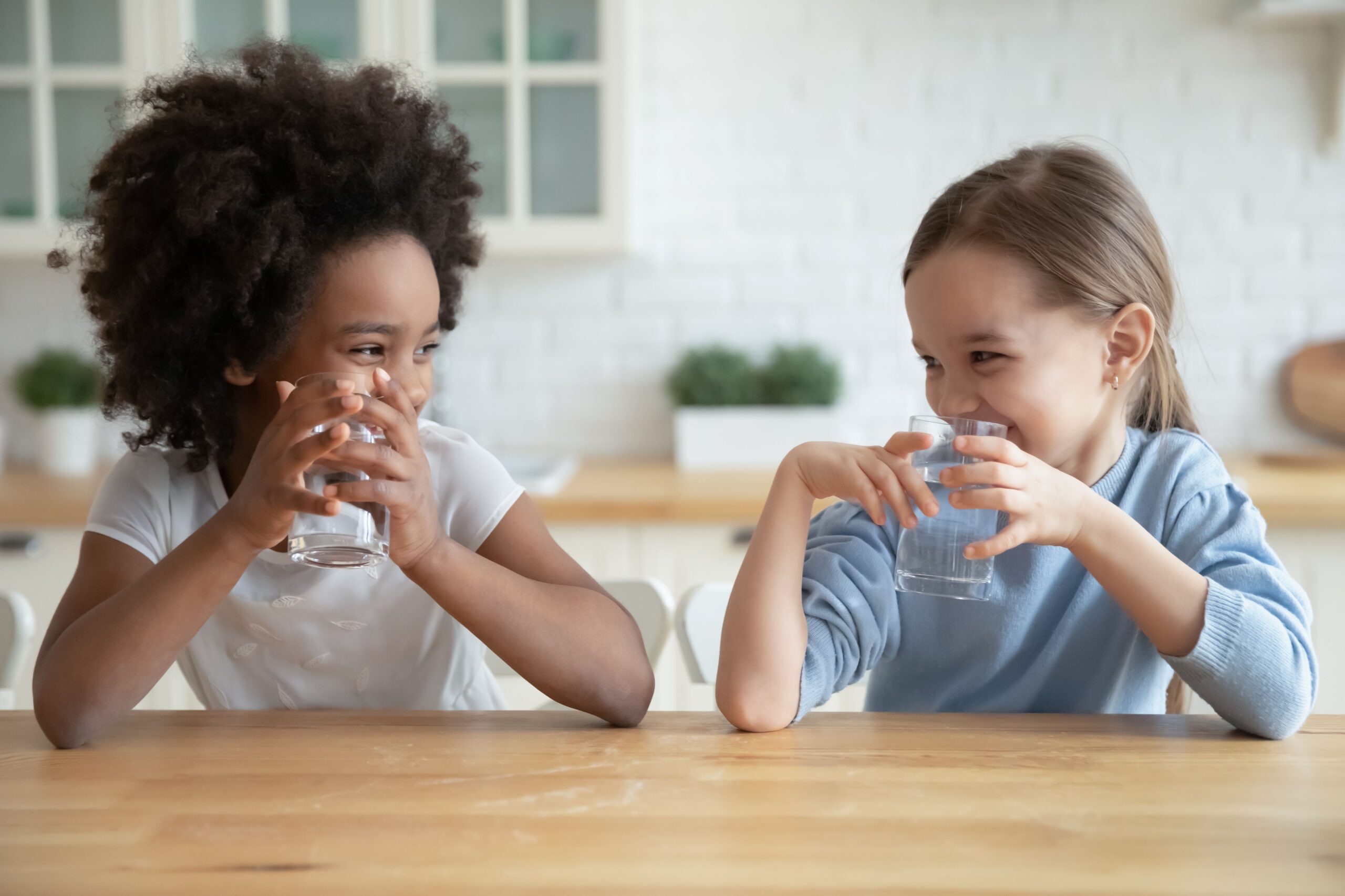 Zwei Kinder trinken lachend Wasser aus Gläsern – Symbolbild für sauberes Trinkwasser durch eine Auftisch Osmoseanlage